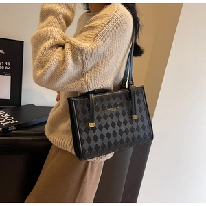 Detail of black quilted tote bag with gold lettering shown on a shoulder