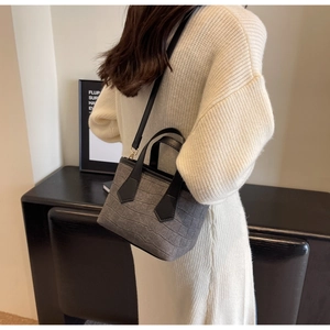Detail of grey crocodile embossed bucket bag with golden hardware and black strap