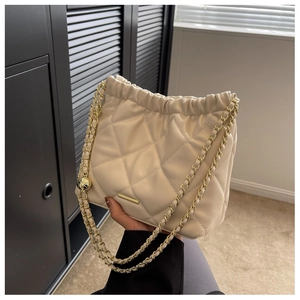 Close-up of cream quilted drawstring bucket bag with gold chain strap held by hand
