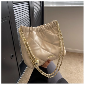 Detail of quilted leather texture and golden metal chain with sphere pendant on handbag