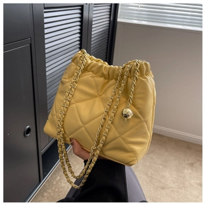 Detailed shot of yellow quilted bucket bag with gold chain and metal ball charm