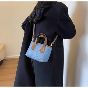 Detailed view of the mini blue textured bucket bag with brown leather straps worn by model