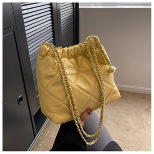 Detail of yellow quilted bucket bag featuring a gold ball chain adjuster and leather strap