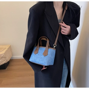 Detailed close-up of blue textured denim tote bag with brown leather handles and strap