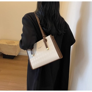 Detail of quilted beige tote bag with brown trim and shoulder strap on model