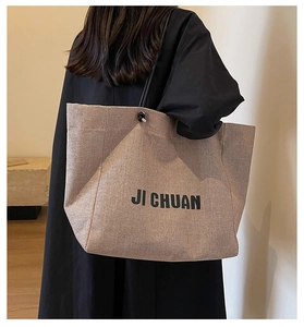 Close-up of khaki canvas tote bag with black logo shown on shoulder of a model