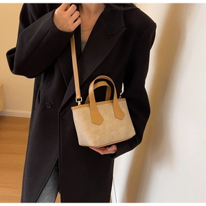 Close-up of a mini beige tote bag with brown handles on a model in a black coat