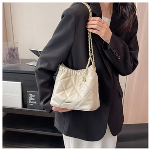 Detail of quilted cream shoulder bag with golden chain and metallic ball accent
