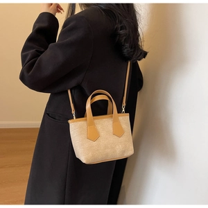 Chic beige textured bucket bag with brown handles worn on a model in a minimalist setting