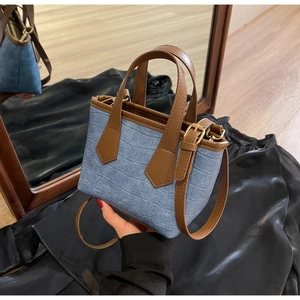 Close-up of blue denim tote bag with crocodile embossing and brown leather handles