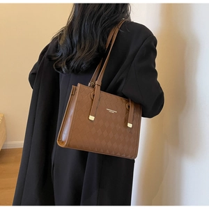 Detailed view of brown quilted tote bag with gold hardware worn by model in black suit