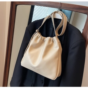 Detail der cremefarbenen Beuteltasche mit Kordelzug und feiner Logo-Prägung am Taschenboden
