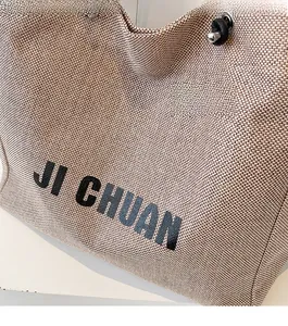 Close-up of beige woven canvas tote bag featuring black JI CHUAN letter print detail