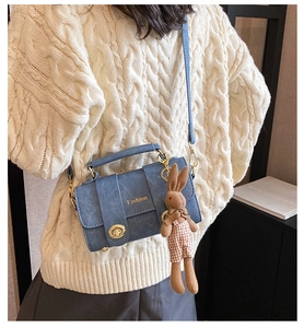 Detail of blue matte leather crossbody bag with gold fashion clasp and plush rabbit charm