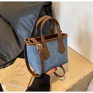 Detail of blue embossed denim bucket bag with brown leather handles and gold hardware