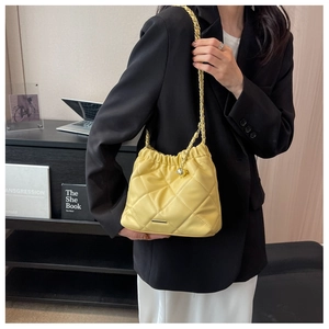 Macro shot of bright yellow quilted bucket bag with gold chain and metal logo detail