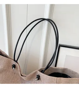 Detail of beige woven tote bag with black knotted rope handles and silver metal tips