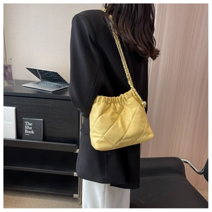 Close-up of yellow quilted chain bag with gold sphere pendant on a chic blazer outfit