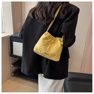 Macro detail of yellow quilted leather bucket bag with golden chain and ball charm
