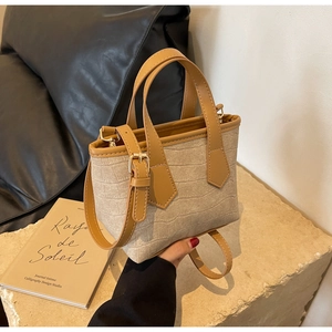 Detail of a beige crocodile textured mini bucket bag with leather handles and gold hardware