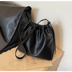 Details einer schwarzen Plissee-Beuteltasche mit Logo auf einem Steinsockel