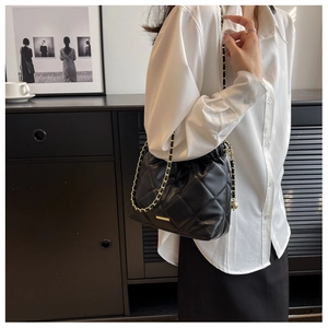 Close-up of black quilted bucket bag featuring a gold chain strap and metal buckle