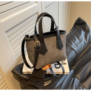 Detail of grey crocodile embossed bucket bag with adjustable black shoulder strap and gold buckle