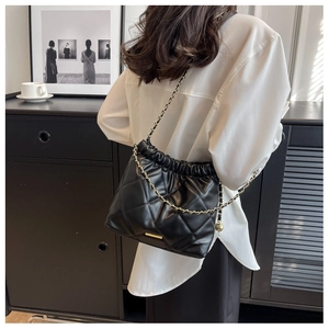 Rear view of model wearing a black quilted bucket bag with gold chain strap