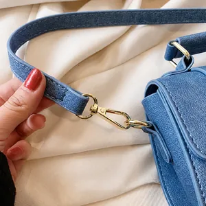 Macro detail of golden spring hook buckle on blue denim crossbody bag with stitching
