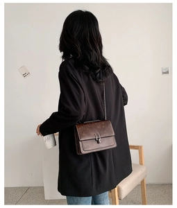 Sac bandoulière en cuir marron avec chaîne et boucle en H porté par un mannequin