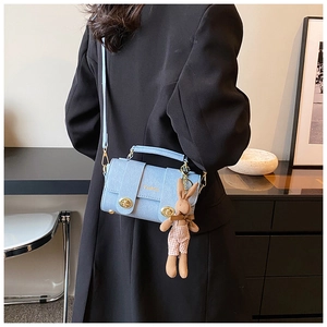 Detail of light blue crossbody bag with dual metal locks and cute rabbit charm on shoulder