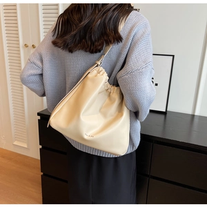 Detailansicht der beigen Plissee-Beuteltasche mit Riemen über einem blauen Pullover
