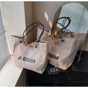 Close-up of khaki canvas tote bag with black handles and JI CHUAN letter printing