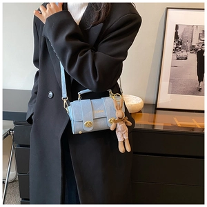 Detail of light blue square bag with denim texture, gold clasp and bunny charm