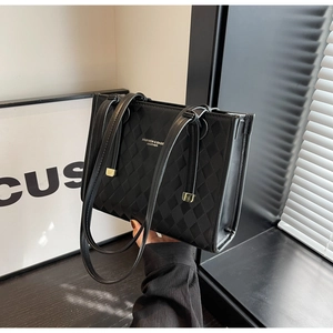 Detail of black quilted tote bag with golden hardware and slim shoulder straps