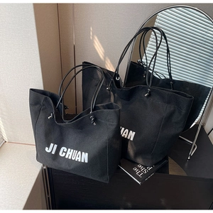 Detail of two black canvas tote bags with white letter prints in an indoor set