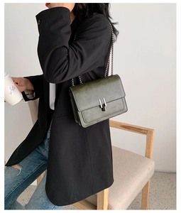 Détail du sac à bandoulière en cuir brillant vert foncé avec chaîne et fermoir en métal
