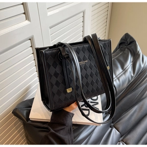 Close-up of black quilted leather tote bag with elegant gold lettering and slim shoulder straps