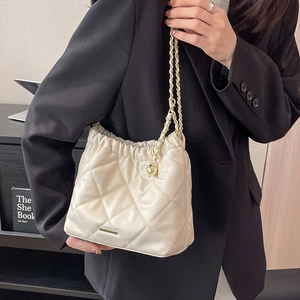 Quilted cream shoulder bag with golden chain and ball charm worn with black suit
