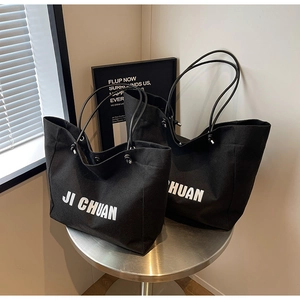 Macro detail of black canvas tote bag showing the white JI CHUAN lettering and metal rivets