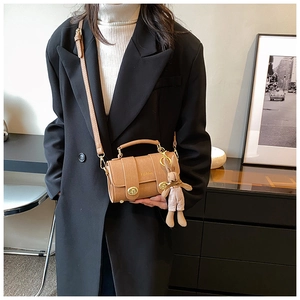 Brown crossbody bag featuring gold hardware and a cute plush bunny charm on black blazer