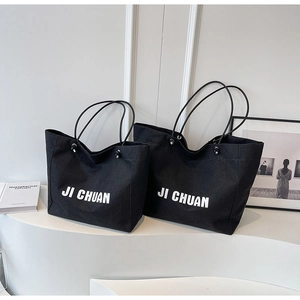 Detail of two black canvas tote bags with JI CHUAN white lettering on minimalist stands