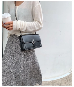 Détail du sac bandoulière noir avec boucle argentée porté par un mannequin en blanc