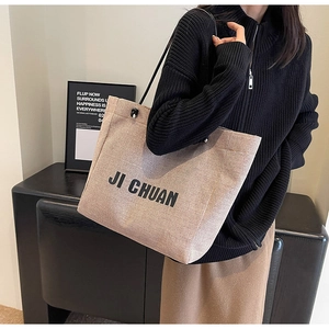 Close-up of beige canvas tote bag with black logo detail and slim shoulder straps