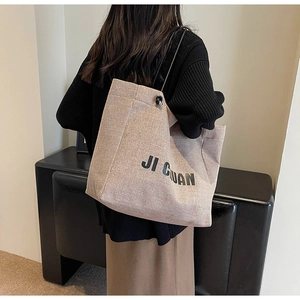Detail of beige canvas tote bag with black JI GUAN lettering and drawstring handles
