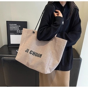 Close-up of beige canvas tote bag with black straps and JI CHUAN logo lettering