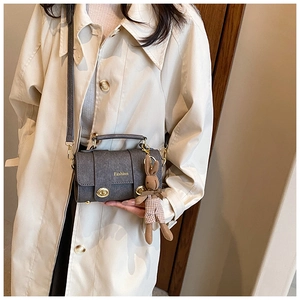 Detail of grey crossbody bag with gold Fashion text, top handle and plush rabbit charm