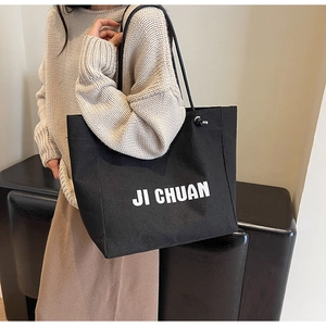 Detail of a large black canvas tote bag with white JI CHUAN print on a female model