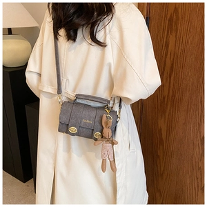 Close-up of grey crossbody bag with gold clasps and cute bunny charm on model