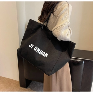 Detail of a large black canvas tote bag with JI CHUAN text carried by a model